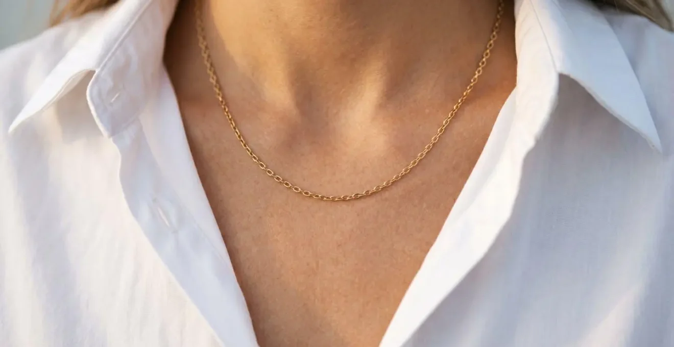 Collier en or fin porté sur peau nue avec chemise blanche entrouverte dans une lumière dorée naturelle