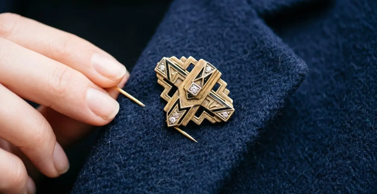 Main tenant délicatement une broche Art Déco dorée sur fond de veste moderne en cachemire bleu marine